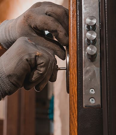 Close-up, the carpenter installs a custom lock in the front metal door, using a drill and hammer and other tools.