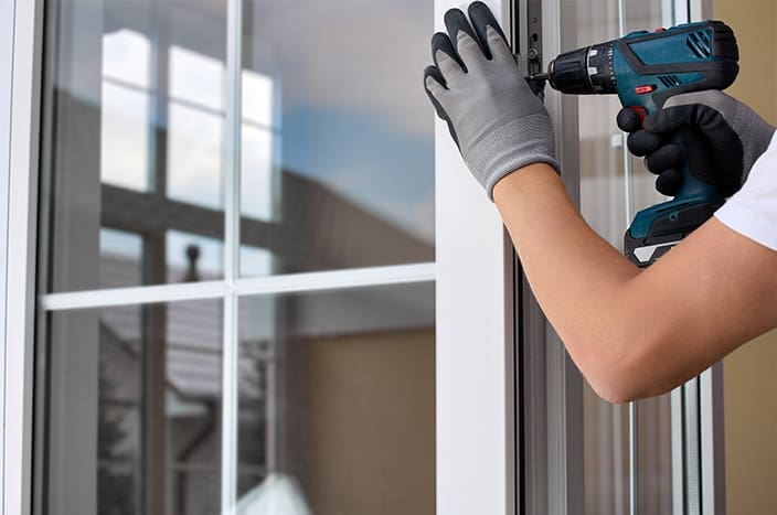Worker's gloved hand with an automatic screwdriver screws the fastening on the plastic door